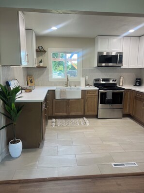 A modern kitchen with white cabinets, a stainless steel microwave, a built-in oven, and a window providing natural light.