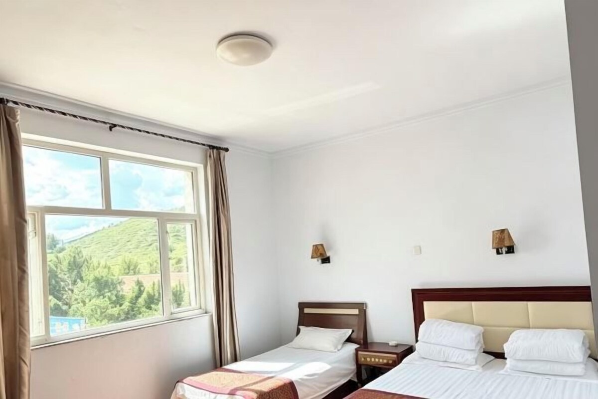 Ein Hotelzimmer mit zwei Betten, einem fenster mit Vorhängen und Blick auf eine grüne Landschaft.