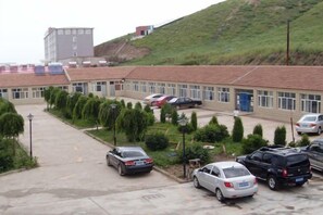 A parking lot with several cars, a building with a red roof, and a hill in the background. - LongYuan Holiday Hotel (Guyuan County)