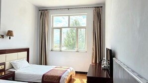 Een slaapkamer met een bed, een bureau, een lamp, een raam met gordijnen en een radiator.