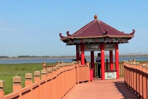 A pavilion with a tiled roof, a wooden walkway, and a view of a body of water. - LongYuan Holiday Hotel (Guyuan County)