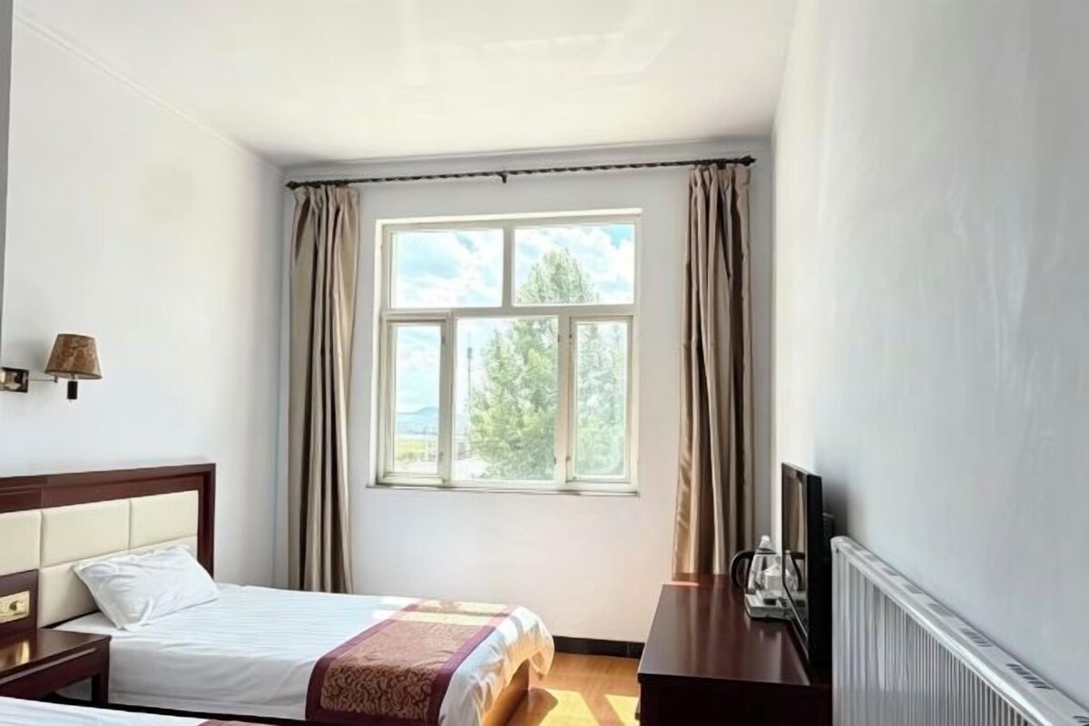 Ein Hotelzimmer mit Bett, Nachttisch, Lampe und einem Fenster mit Vorhängen.