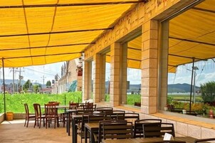 An outdoor seating area with tables and chairs under a yellow canopy, overlooking a green landscape.