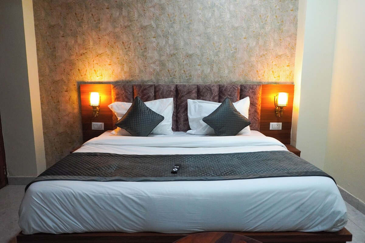Cama bem arrumada com roupa de cama branca e verde escuro, duas luminárias fixadas na parede e uma parede texturizada atrás da cama.