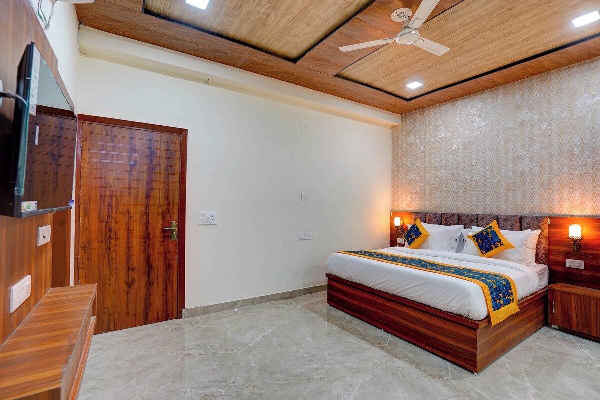 A bedroom with a wooden ceiling, a bed with a patterned headboard, bedside lamps, and a TV mounted on the wall.