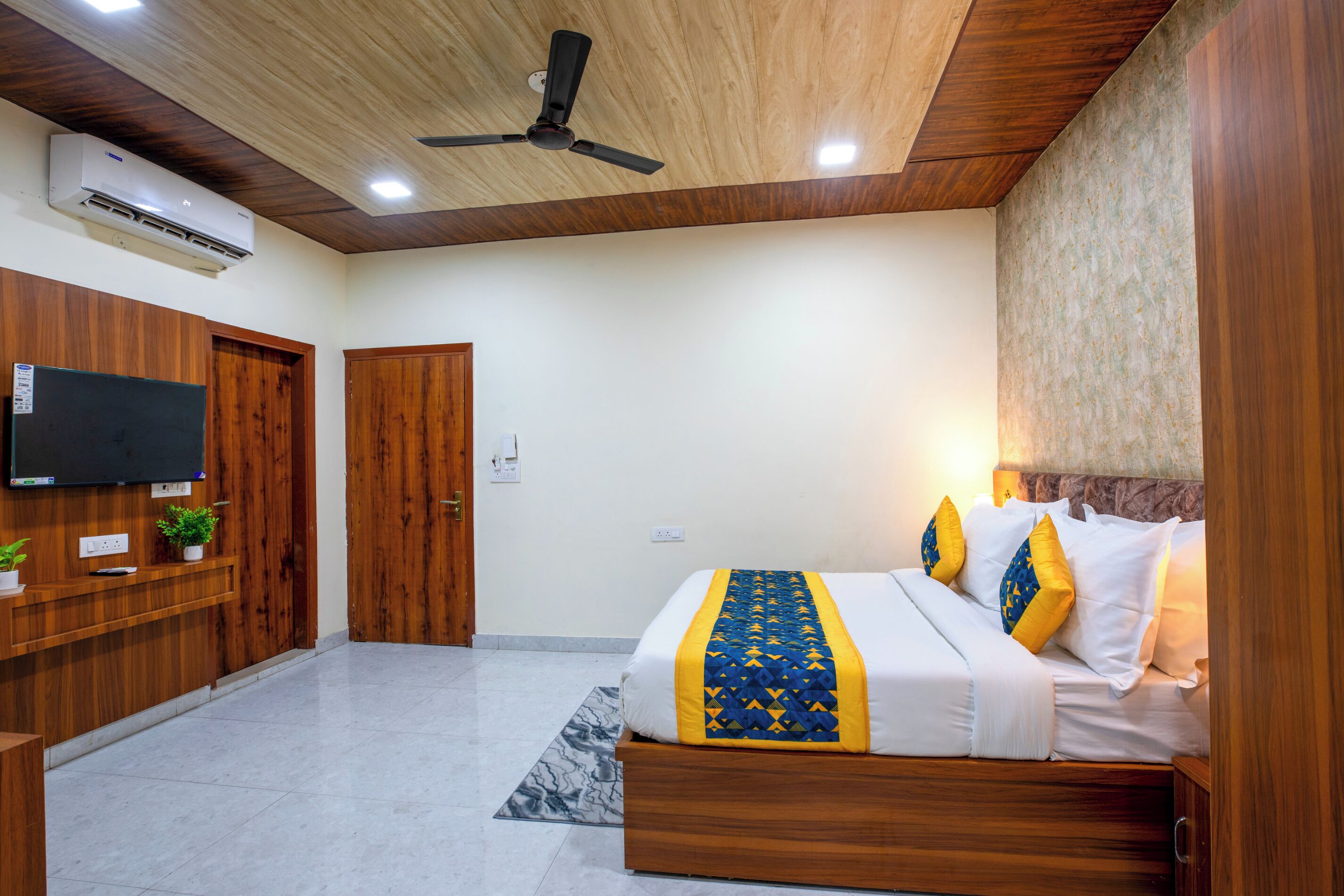 Une chambre à coucher avec un lit, des lambris en bois, un ventilateur de plafond, une télévision et une petite plante.