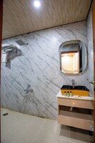 Une salle de bain avec un mur en marbre, une douche, un lavabo avec des articles de toilette et un miroir.