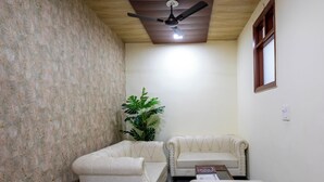 A corner room with a ceiling fan, two sofas, a small table, and a potted plant. - Aarchh Royale (Noida)