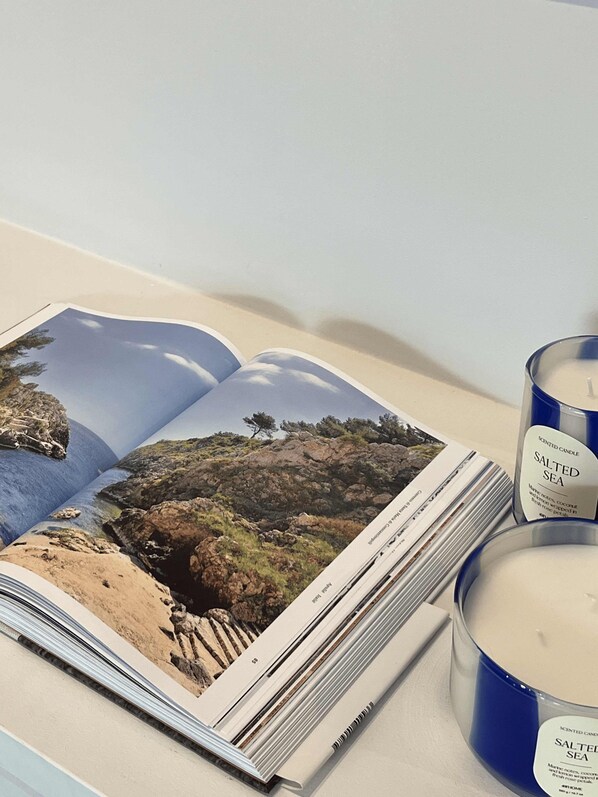 An open magazine with a coastal landscape photo, a blue candle labeled "Salted Sea," and a white candle on a table.
