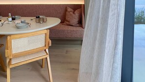 A modern room with a round dining table, wooden chairs, a sofa with cushions, a hanging light fixture, and a large window with a curtain. - Huswell - Nosso Logies - Chic Stay in Knokke-heist (Knokke-Heist)