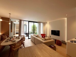 A modern living room with a dining area, a sofa, a TV mounted on the wall, and a sliding glass door leading to a balcony.