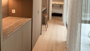 A narrow hallway with wooden flooring, a small stool, and a bed in the background. - Huswell - Nosso Logies - Chic Stay in Knokke-heist (Knokke-Heist)