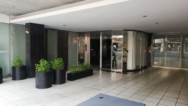 Una entrada moderna de edificio con puertas de vidrio, plantas en macetas y piso de baldosas.