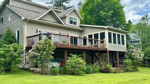 A two-story house with a deck, surrounded by a well-maintained lawn and various plants.