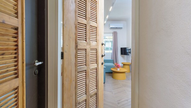A hallway with a wooden door, a light-colored wall, and a modern interior with a sofa and a round yellow table. - Tulip 2BR Apartment In Gemmayze (Bayrut)