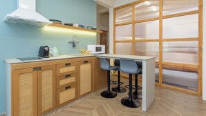 A compact kitchen with a microwave, kettle, and toaster on the counter, a wooden cabinet with drawers, and a bar stool area. - Tulip 2BR Apartment In Gemmayze (Bayrut)