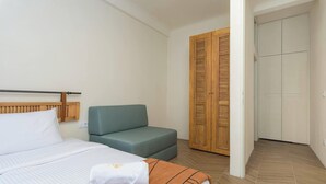 A hotel room with a bed, a sofa, a wooden wardrobe, and a door leading to another room. - Tulip 2BR Apartment In Gemmayze (Bayrut)