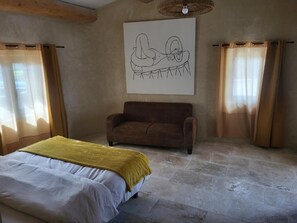 Une chambre à coucher avec un lit, un canapé marron, une grande œuvre d’art accrochée au mur et des rideaux aux fenêtres.