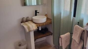 Une salle de bain avec un lavabo rond, un miroir, un porte-serviettes et une poubelle.
