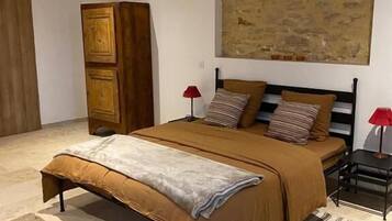 A bedroom with a bed, a nightstand, a red lamp, a wooden wardrobe, and a large abstract painting on the wall.