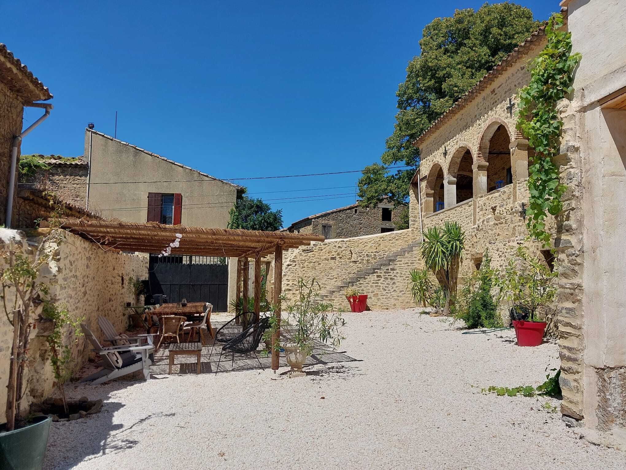 Ein Innenhof mit Steingebäuden, einer Pergola, Sitzmöglichkeiten im Freien und Kübelpflanzen.
