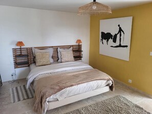 A bedroom with a wooden headboard, a bed with striped bedding, two bedside lamps, a woven light fixture, and a wall-mounted artwork of a cow. - bastide de la madeleine (Pougnadoresse)