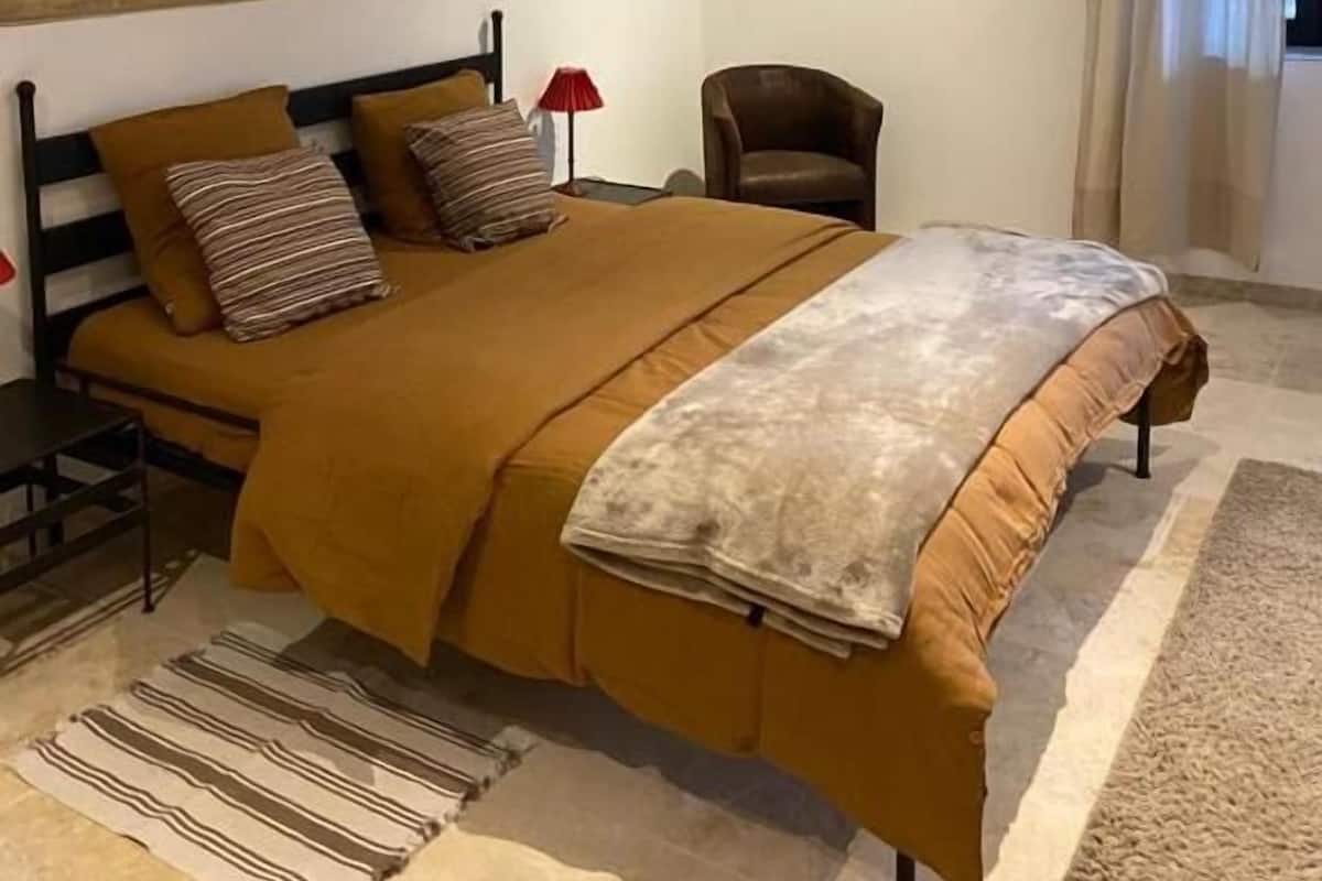 A bedroom with a large bed, a chair, a painting, and an air conditioning unit.