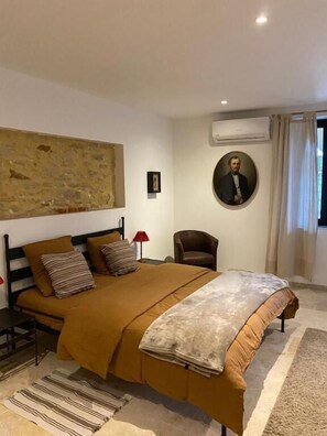 A bedroom with a large bed, a chair, a painting, and an air conditioning unit. - bastide de la madeleine (Pougnadoresse)