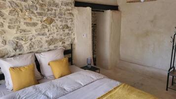 A bedroom with a stone wall, a bed with white and yellow bedding, a bedside table with a lamp, and a hanging light fixture.