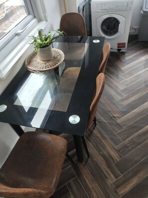 A dining area with a glass-top table, brown chairs, a potted plant, and a washing machine in the background. - Central Angel Location: 1BR Apartment (Greater London)