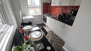 A compact kitchen with a dining area, featuring a window, a red-tiled backsplash, and a modern stove. - Central Angel Location: 1BR Apartment (Greater London)
