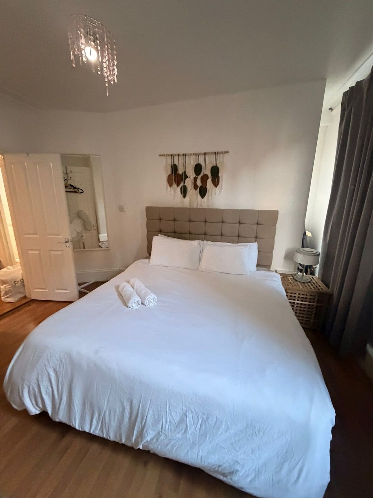 A large bed with white linens, a tufted headboard, and a wall-mounted art piece.