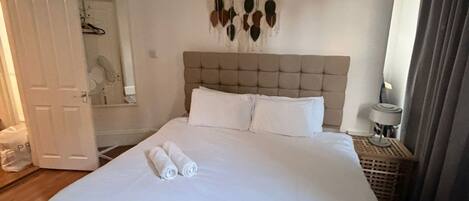 A large bed with white linens, a tufted headboard, and a wall-mounted art piece.