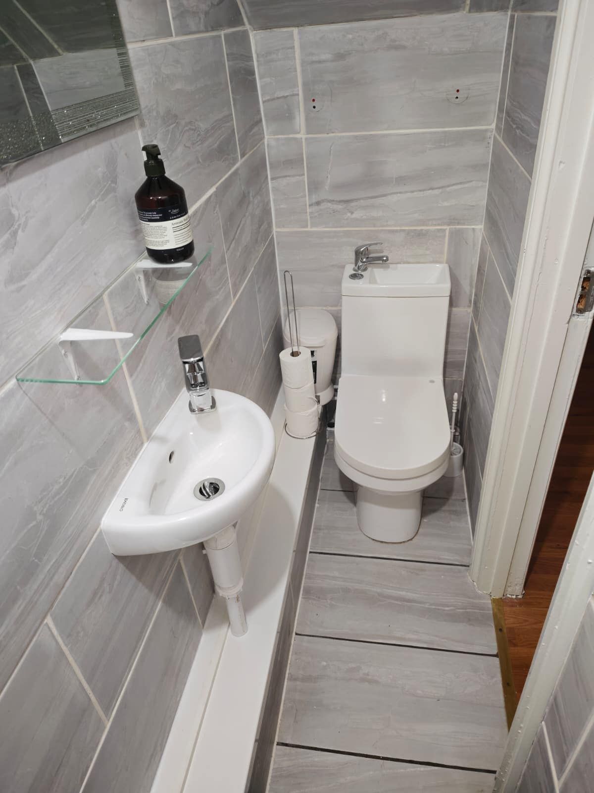 A small, modern bathroom with a white sink, toilet, and glass shelf.
