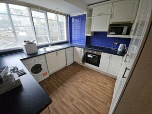 A compact kitchen with a washing machine, microwave, and oven.