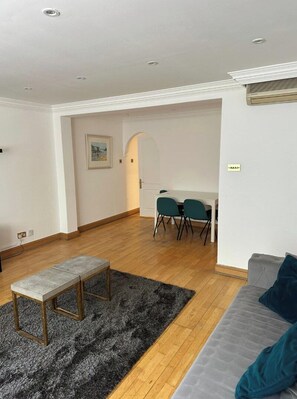 Un salon moderne avec un canapé gris, un petit banc en bois et un coin repas comprenant une table et des chaises.