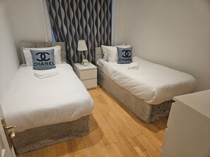 A hotel room with two single beds, a nightstand with a lamp, and a patterned wall.