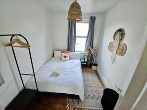 Une petite chambre à coucher, bien rangée, avec un lit, un luminaire suspendu, une table de chevet et un objet décoratif fixé au mur.