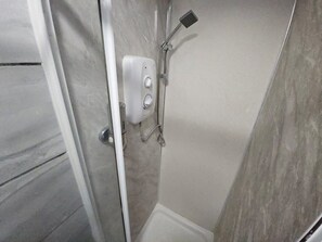 A shower area with a handheld showerhead, a control panel, and a wall-mounted faucet.