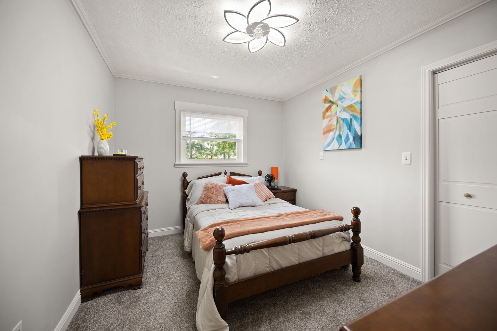 A bedroom with a wooden bed, a dresser, a nightstand, a window, and a ceiling fan.