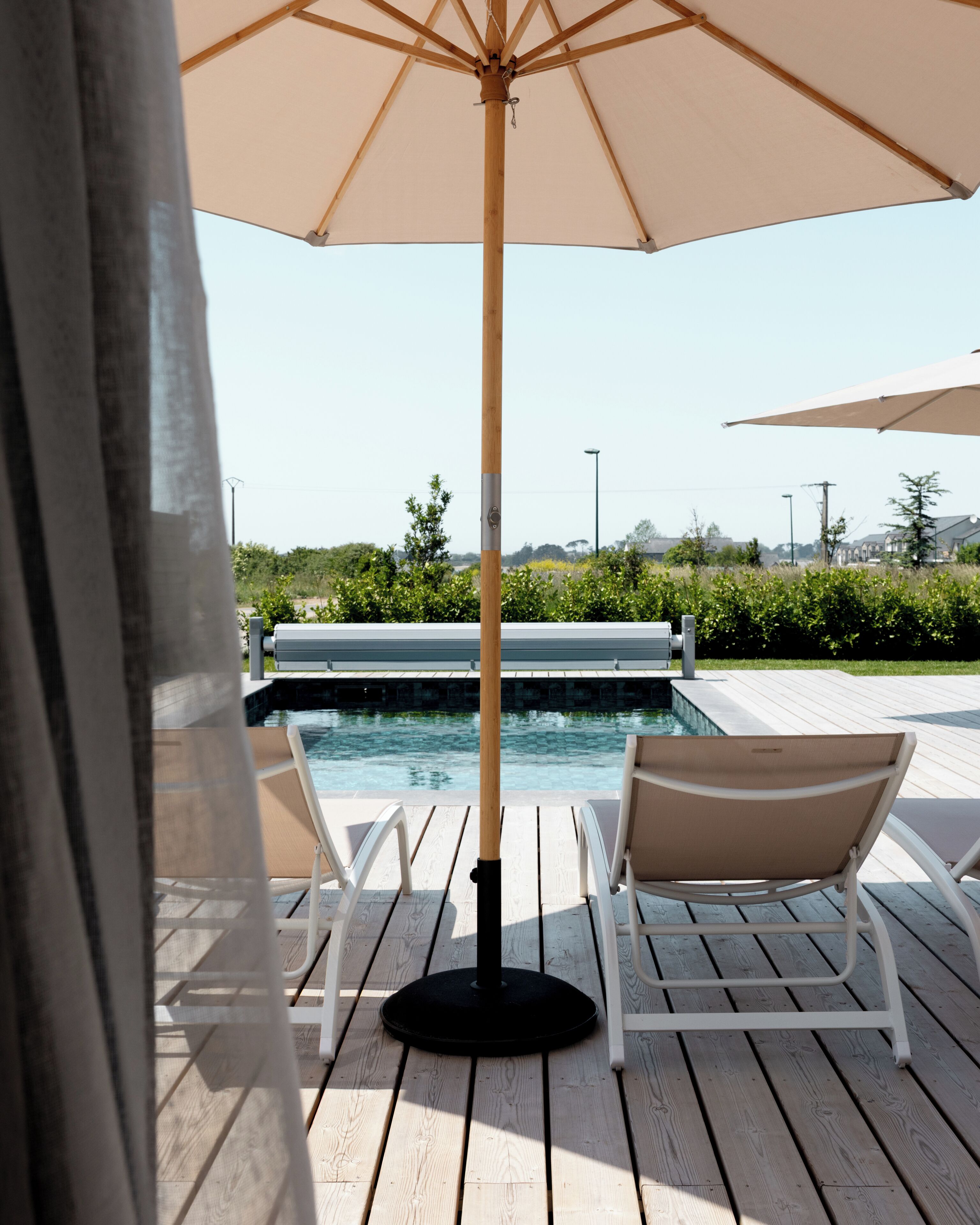 Un espace aménagé au bord de la piscine, avec une terrasse en bois, des chaises longues et un grand parasol.