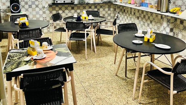 A dining area with multiple tables and chairs, an air conditioning unit, and a tiled backsplash. - Hotel Naciuonal (Sobral)