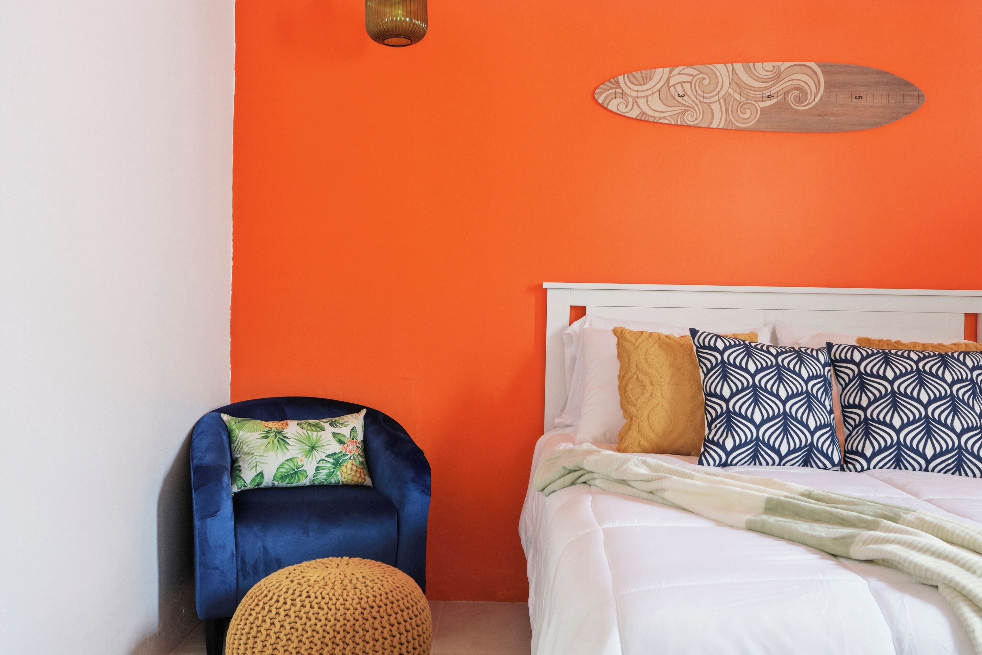 Une chambre à coucher avec un lit, un fauteuil bleu et un pouf rond.