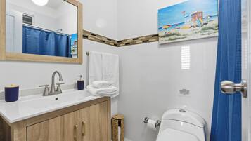 Een badkamer met een houten kast, een witte wastafel en een schilderij van een strand.
