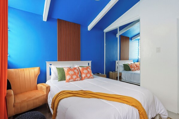 A hotel room with a large bed, a wooden chair, and a mirror.
