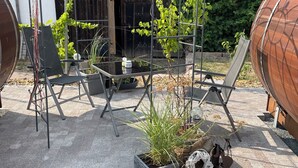 Ein Patio mit Metall-Pergola, zwei Stühlen, einem Tisch und Kübelpflanzen.