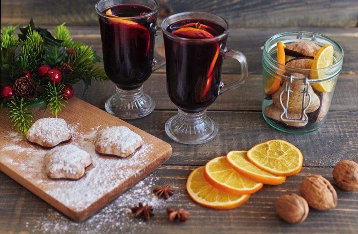 Deux verres de vin chaud, un bocal en verre contenant des noix et des tranches d’orange, et une planche en bois avec des biscuits.