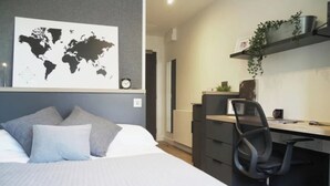 Una camera da letto con un letto, una scrivania e una sedia. C'è una mappa del mondo appesa al muro e una sveglia sul comodino.