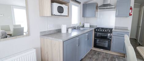 A modern kitchen with grey cabinets, a built-in microwave, a stove, and a sink.