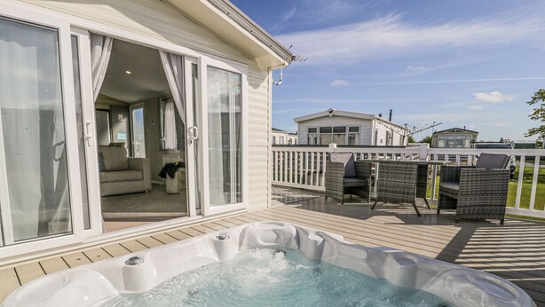 A hot tub on a wooden deck with a sliding glass door leading to a living area. - Manor House Platinum 3 Bedroom (Maryport)